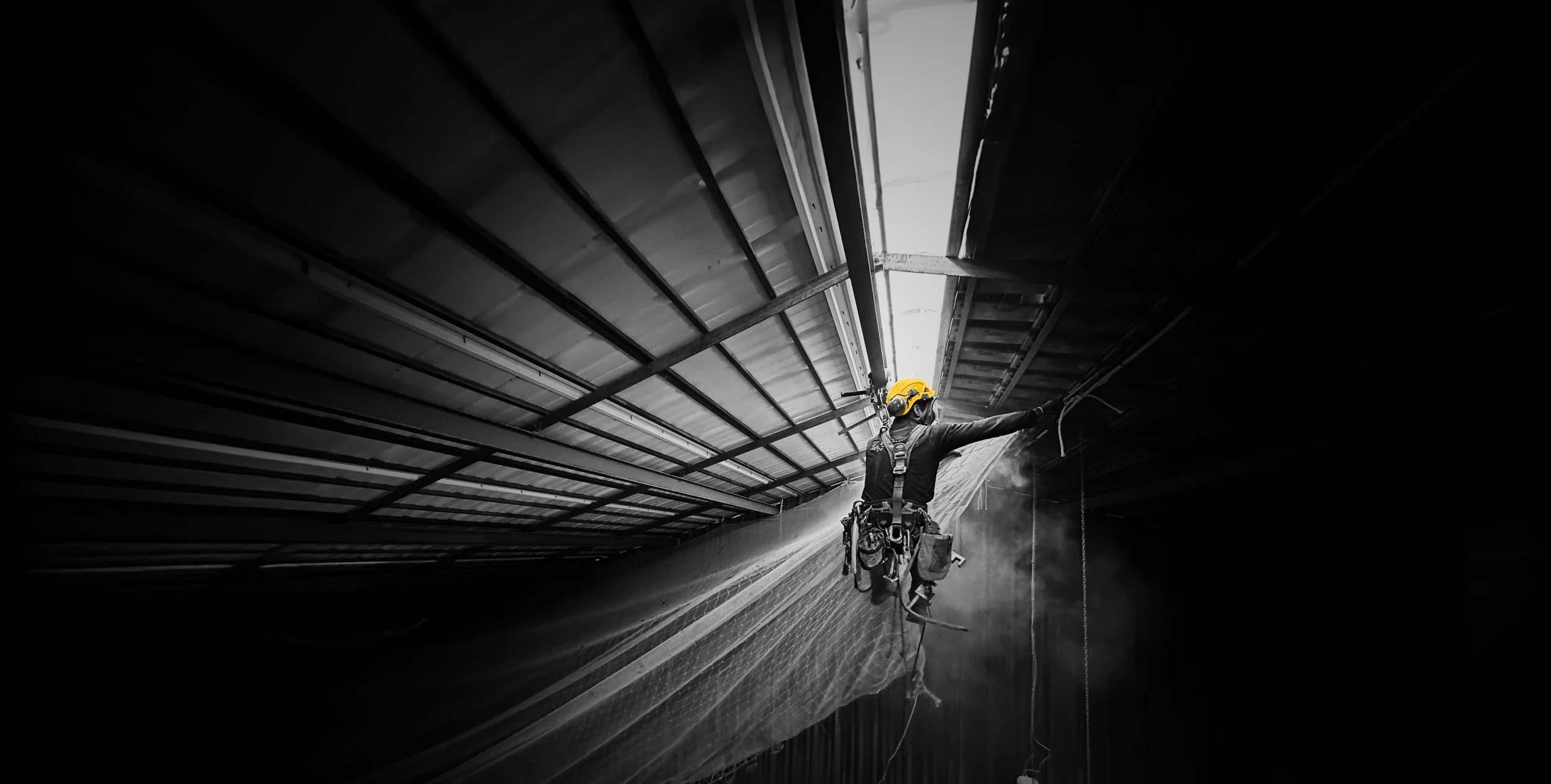 Technicien cordiste sécurisé posant un filet en hauteur sous charpente métallique industrielle