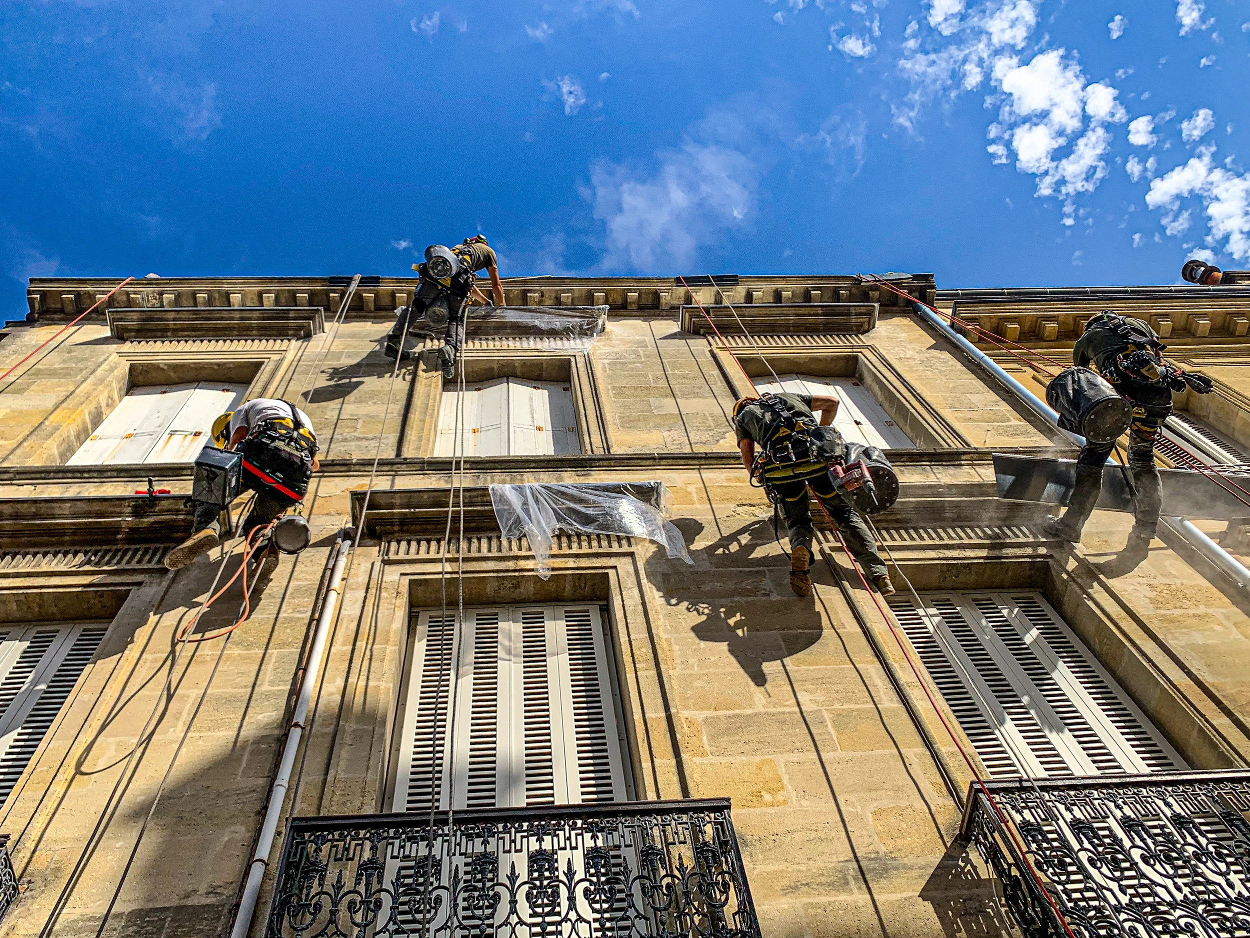 Techniciens cordistes en accès sur corde réalisant des travaux de façade sur immeuble en pierre.