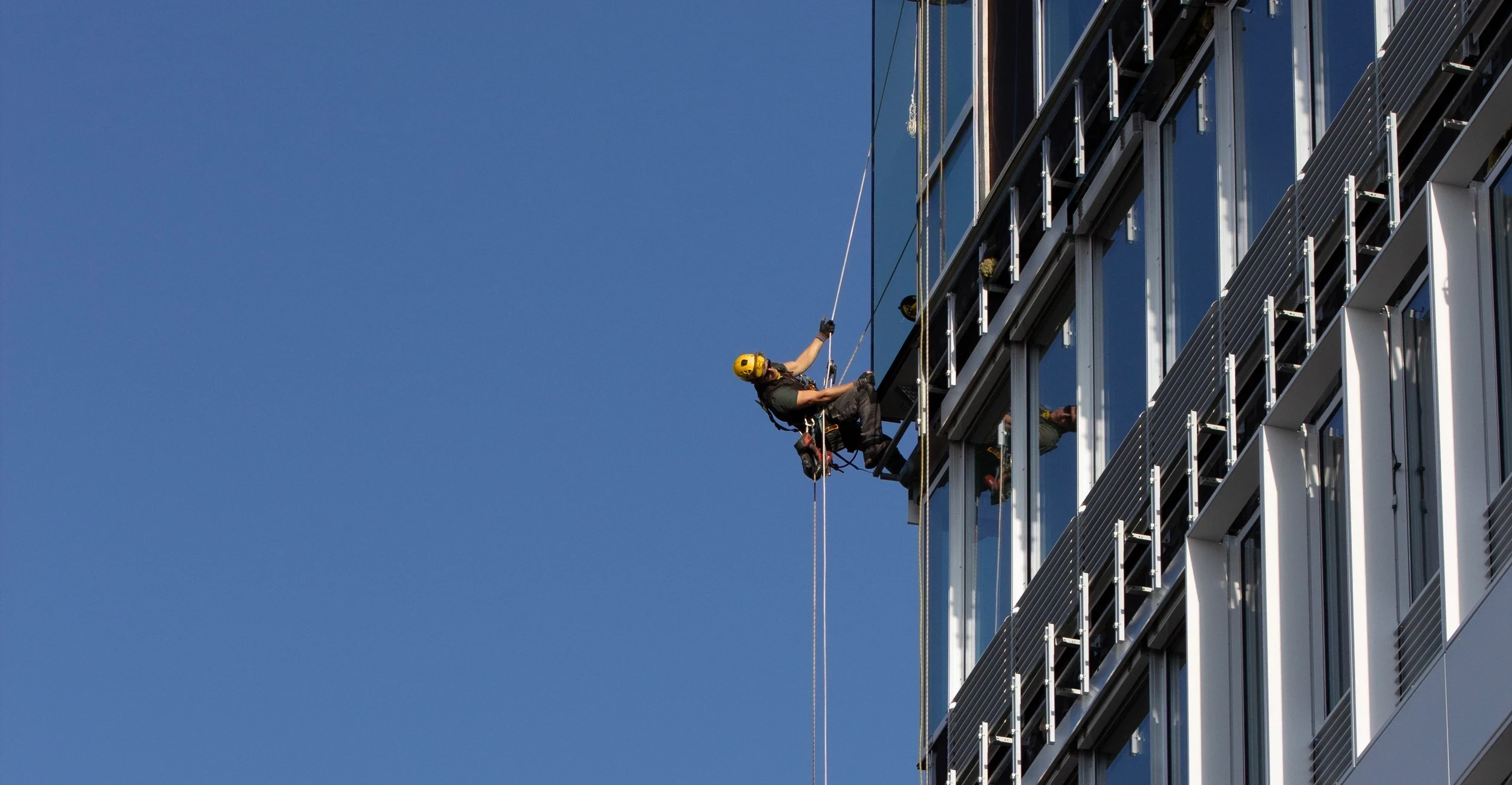 Technicien cordiste sécurisé intervenant sur façade vitrée d’immeuble pour travaux en hauteur